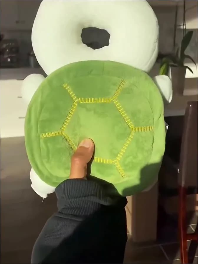 Het groene, schildpadvormige MoshiGuard valkussen van dichtbij, een hand drukt in de zachte vulling